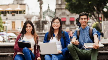 Three students sitting outside with their laptops.