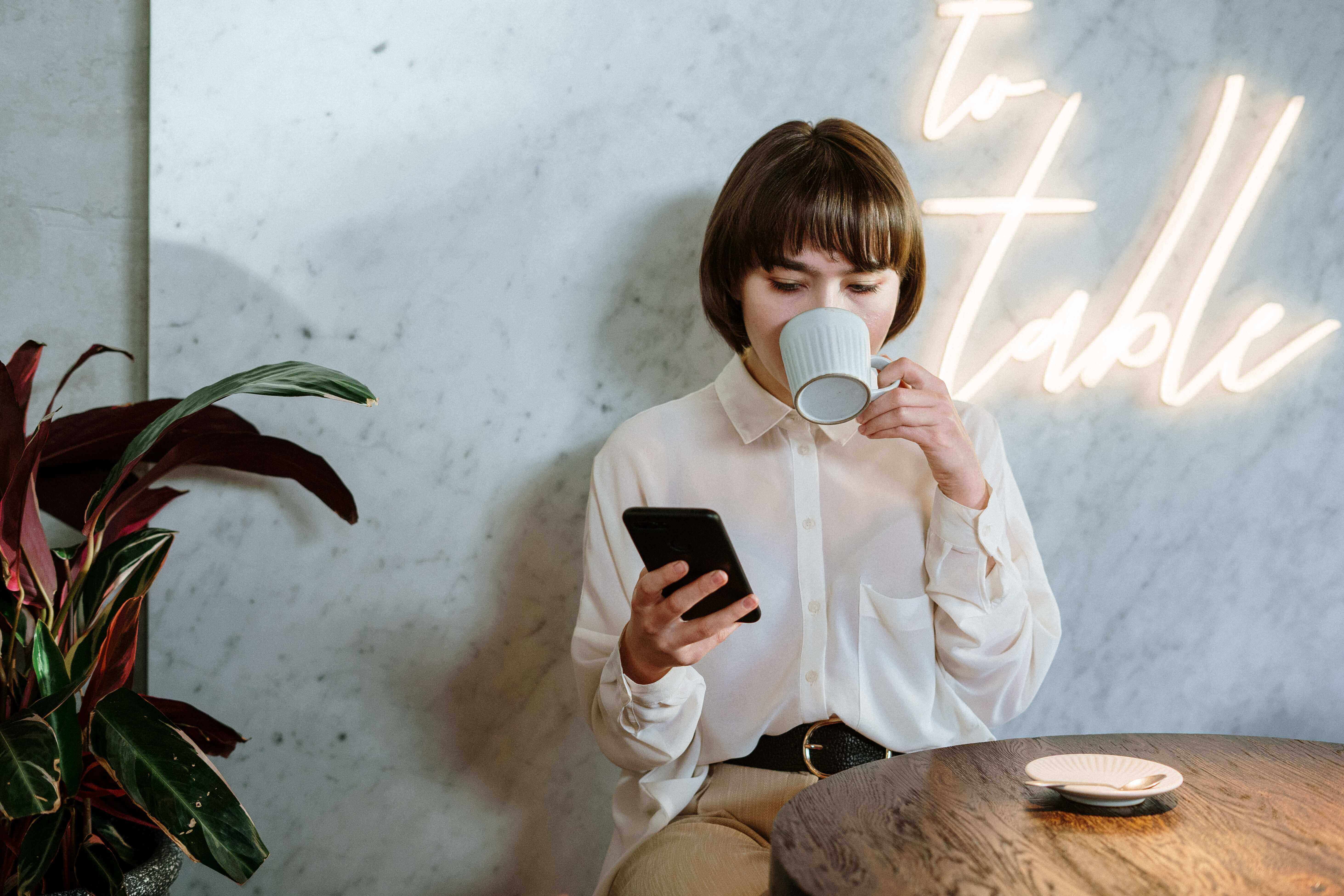 a woman drinking a coffee while looking at an app on her phone