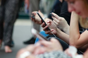 A person looking at their phone in a crowd. The photo is focused on the phone and hands with everyone else blurred out