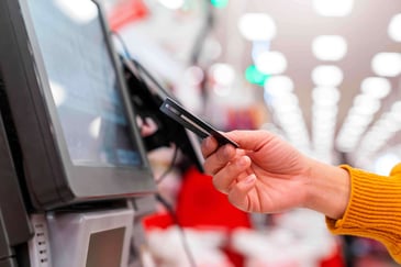 A person tapping their credit card at a retail self-checkout kiosk