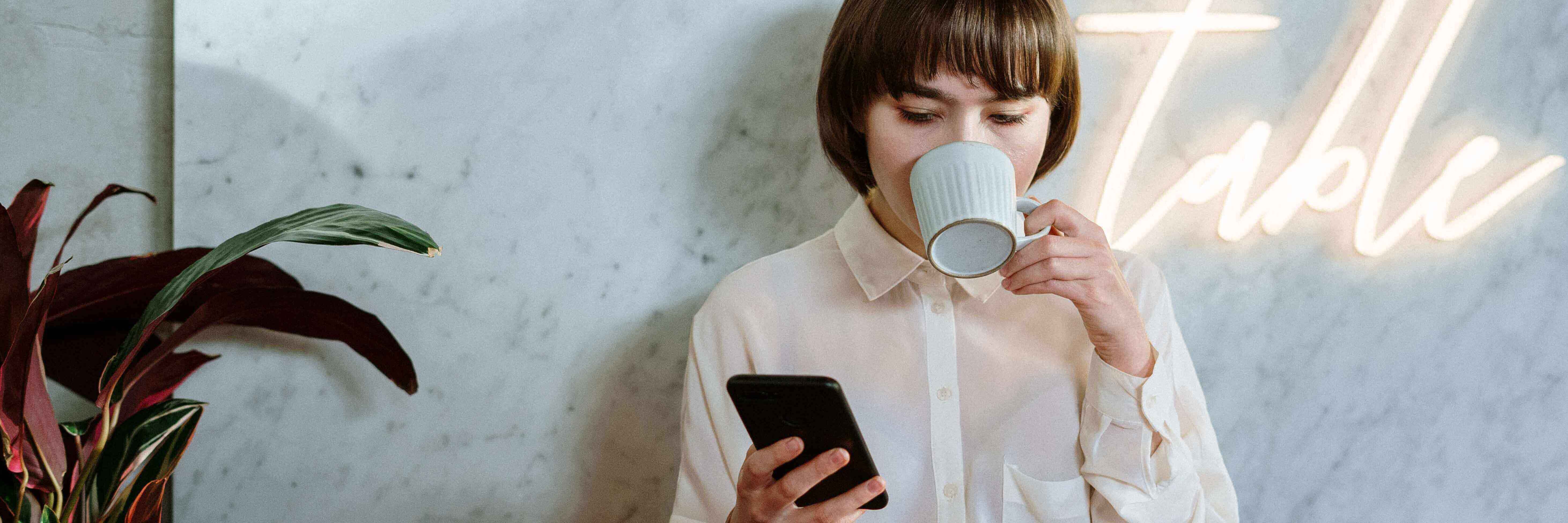 A woman drinking coffee while looking at her phone