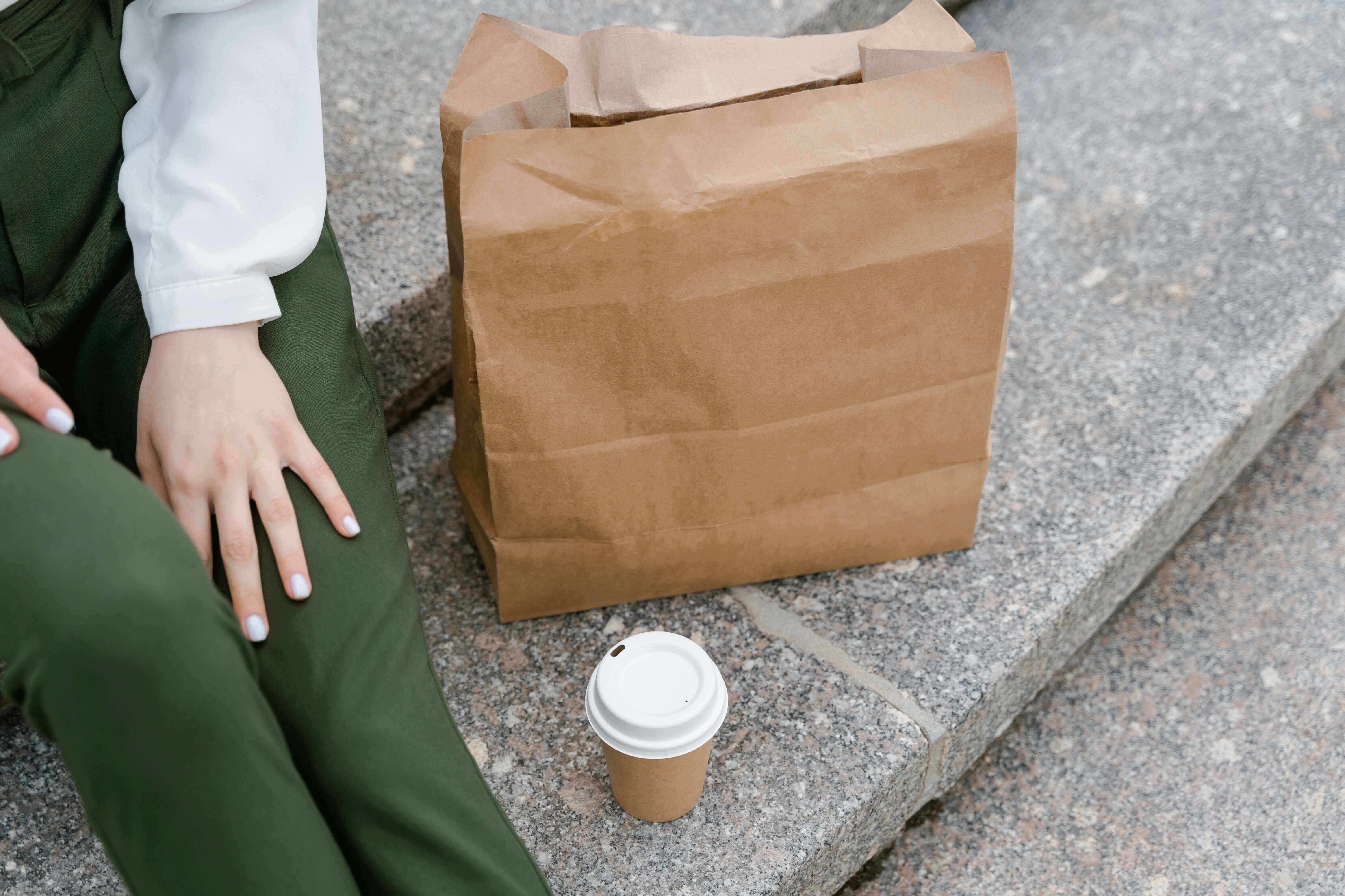 A woman sitting beside a takeout bag and a coffee