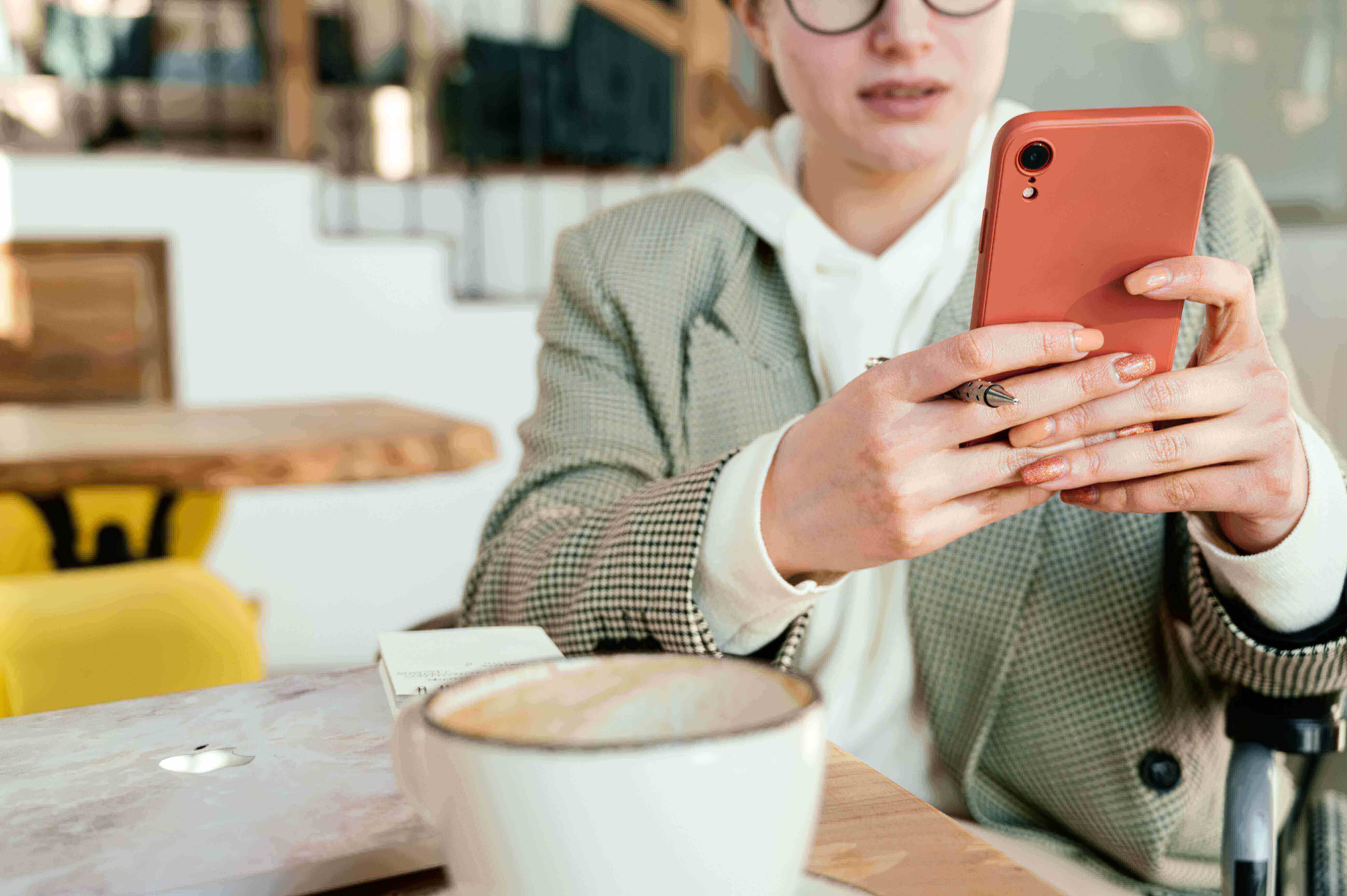 A woman sitting at a cafe holding a pink phone in front of her