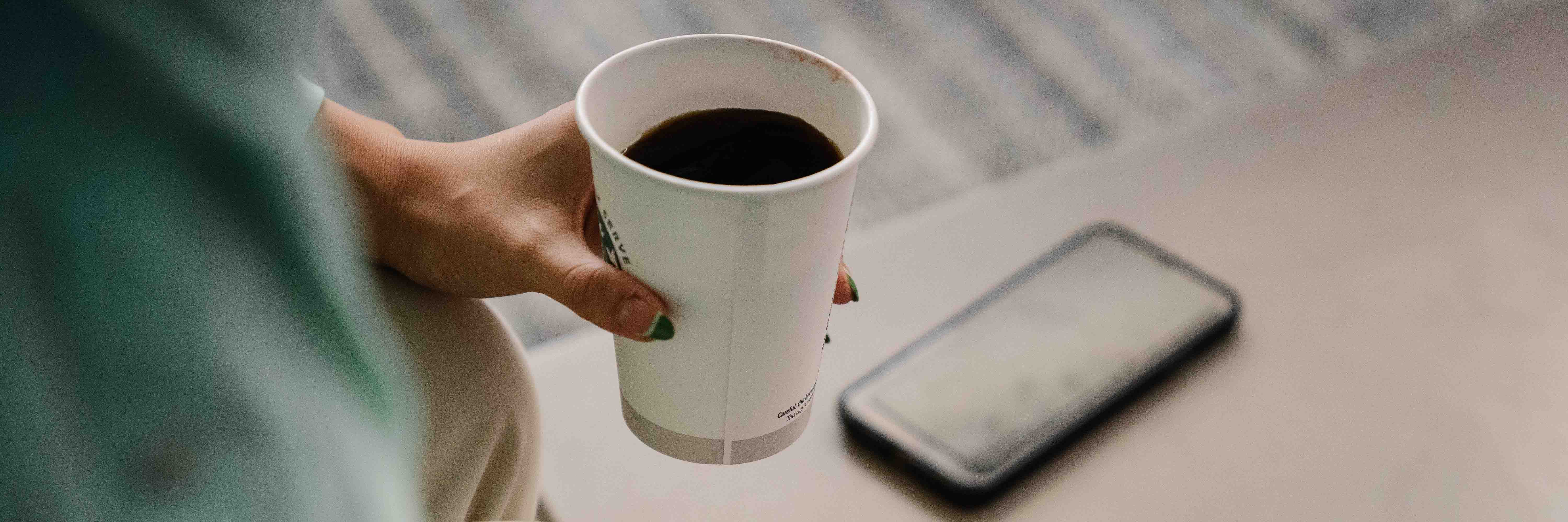 A cup of coffee held next to a phone on the table